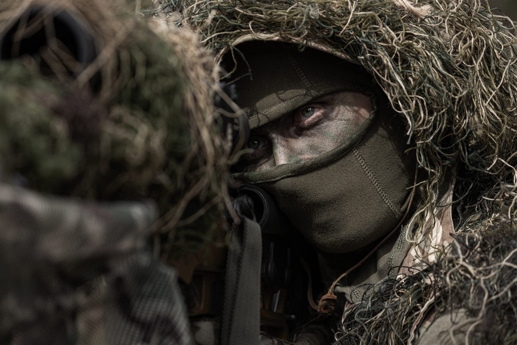 Sniper in a ghillie suit, eyes behind the scope