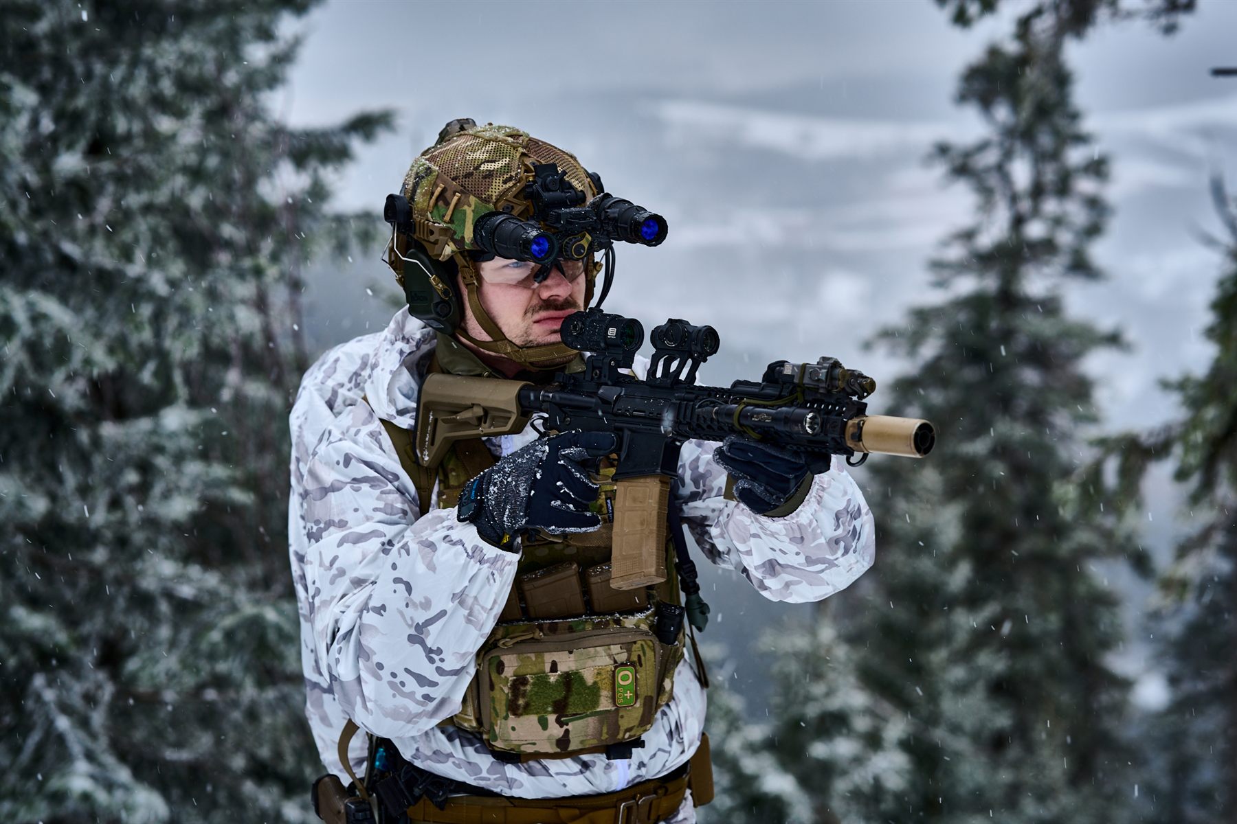 Operator in winter camouflage with night-vision goggles in a snowy forest