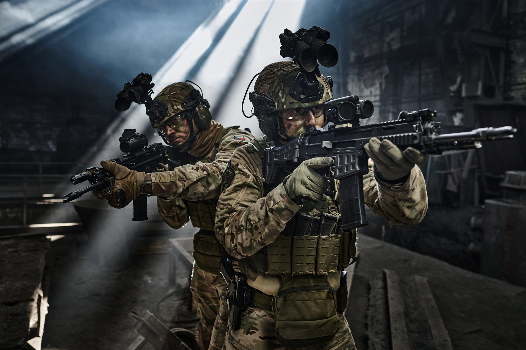 Two soldiers with night-vision mounts aiming carbines in an industrial hall