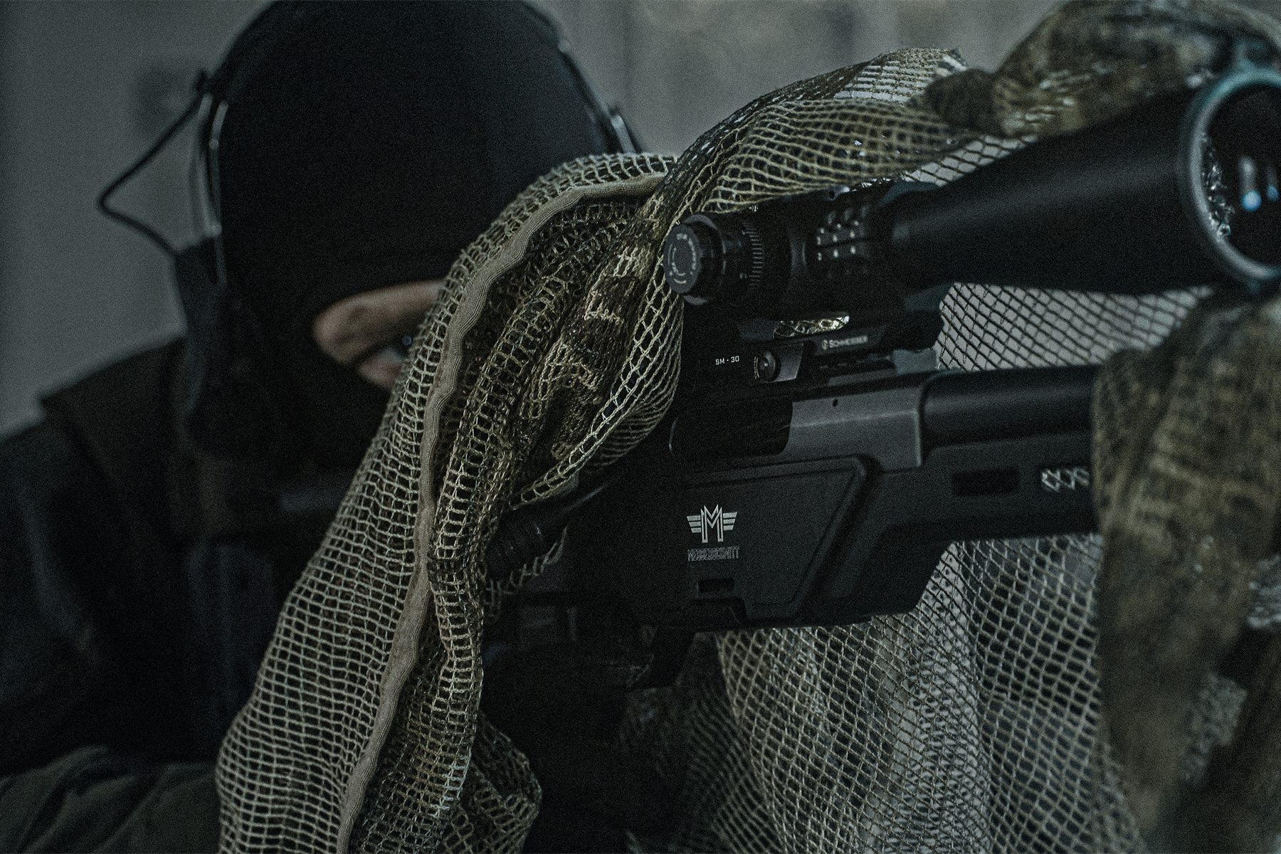 Riflescope in close-up with the shooter behind it